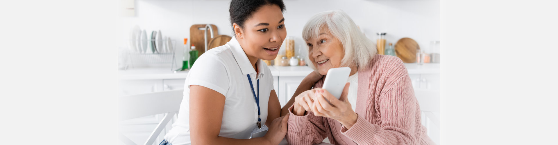 happy senior woman showing smartphone to amazed multiracial social worker at home
